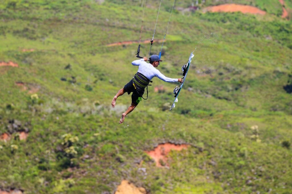 A kitesurfer executes an impressive aerial maneuver above a lush green landscape, capturing the essence of adventure and freedom.