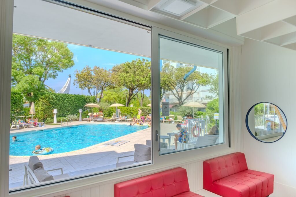 View of a vibrant summer pool scene from a stylish indoor hotel lounge.